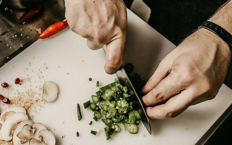Hands slicing green chilli on a white board