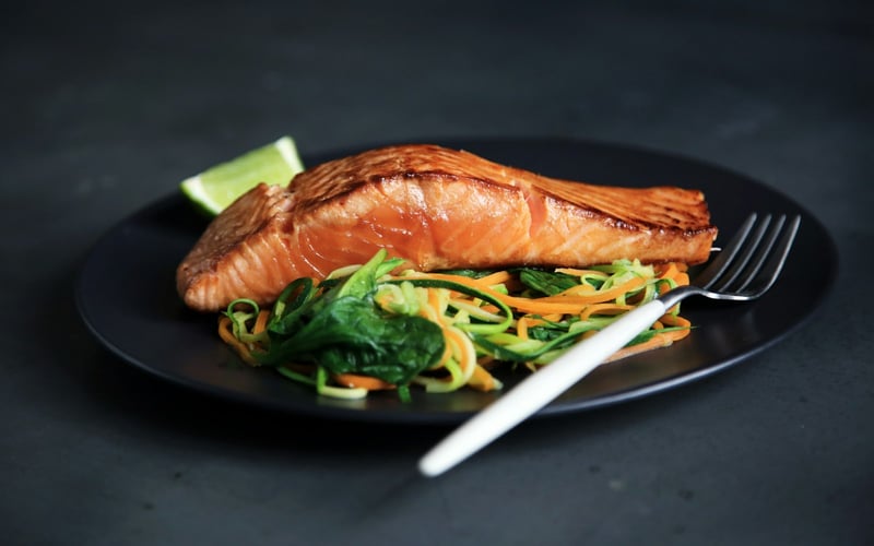 Seared salmon on a dark plate with ribboned vegetables